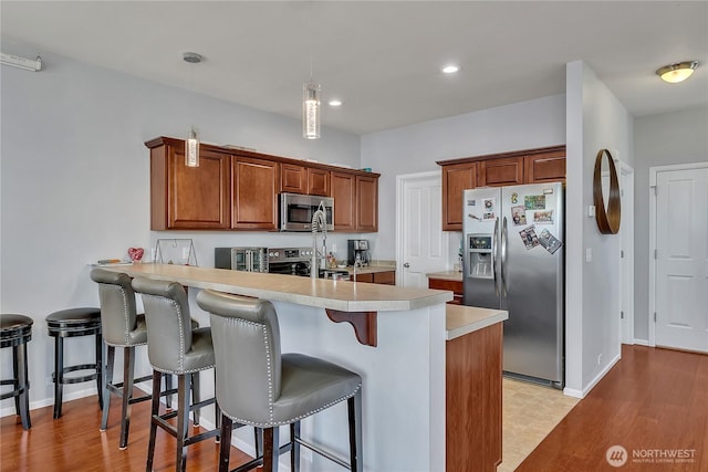 4023 Tribute Ave E, Fife, WA 98424 - kitchen featuring stainless steel appliances, a peninsula, light countertops, a kitchen breakfast bar, and light wood-style flooring