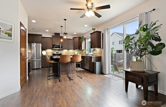 14410 99th Way SE, Yelm, WA 98597 - kitchen featuring stainless steel appliances, dark brown cabinetry, a kitchen island, a kitchen breakfast bar, and decorative backsplash