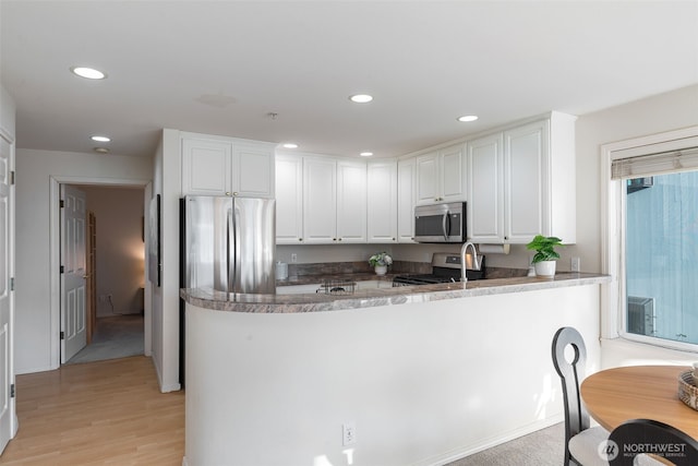 2241 13th Ave W, Seattle, WA 98119 - kitchen with stainless steel appliances, white cabinets, recessed lighting, light wood-style flooring, and a peninsula