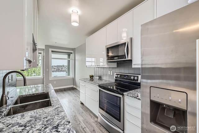 655 Crockett St Unit B304, Seattle, WA 98109 - kitchen with stainless steel appliances, backsplash, light stone counters, white cabinetry, and light wood-style flooring