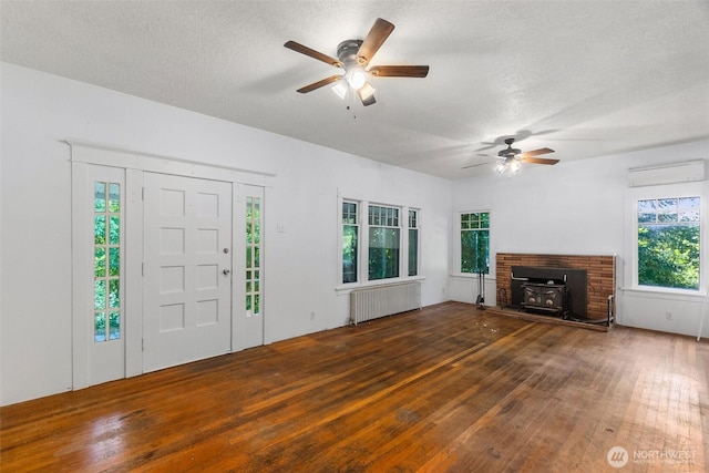 212 SE Cowlitz Rd, Winlock, WA 98596 - unfurnished living room featuring radiator heating unit, a wood stove, a wall mounted air conditioner, ceiling fan, and a textured ceiling