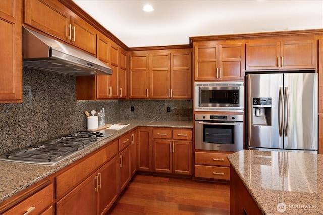 1206 S 36th Pl, Renton, WA 98055 - kitchen featuring stainless steel appliances, under cabinet range hood, brown cabinets, dark wood-type flooring, and backsplash