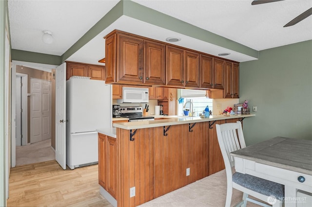 1541 Sheridan Unit C2, Bremerton, WA 98310 - kitchen with white appliances, a kitchen breakfast bar, light wood-style flooring, a ceiling fan, and brown cabinetry
