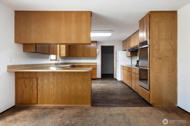 1078 NW Kitsap Ter, Oak Harbor, WA 98277 - kitchen featuring a peninsula, under cabinet range hood, brown cabinetry, and light countertops