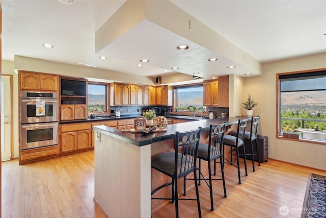 622 Vista View Pl, East Wenatchee, WA 98802 - kitchen featuring stainless steel double oven, light wood-style floors, dark countertops, tasteful backsplash, and recessed lighting
