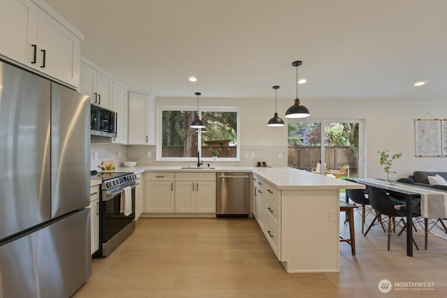 10342 39th Ave NE, Seattle, WA 98125 - kitchen featuring stainless steel appliances, a peninsula, light wood-style flooring, tasteful backsplash, and white cabinetry