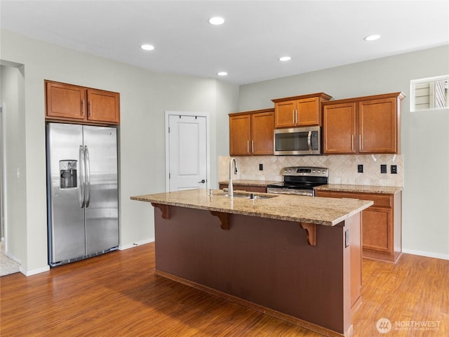 2220 166th St Ct E, Tacoma, WA 98445 - kitchen featuring stainless steel appliances, wood finished floors, brown cabinets, decorative backsplash, and a kitchen bar