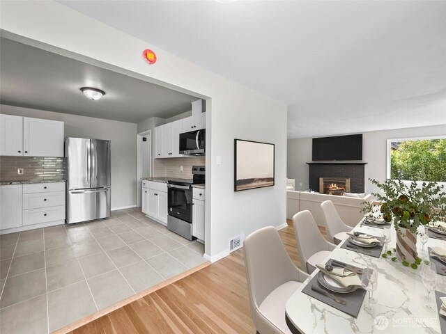 4510 N 24th St, Tacoma, WA 98406 - kitchen featuring appliances with stainless steel finishes, decorative backsplash, white cabinetry, and a fireplace