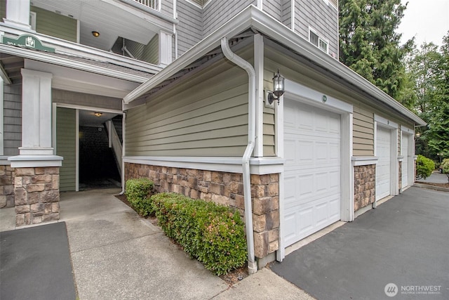 12712 Admiralty Way Unit F106, Everett, WA 98204 - view of property exterior with stone siding, an attached garage, and asphalt driveway