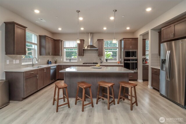 16321 SE 133rd Pl, Renton, WA 98059 - kitchen with appliances with stainless steel finishes, wall chimney exhaust hood, a center island, a kitchen bar, and light wood finished floors