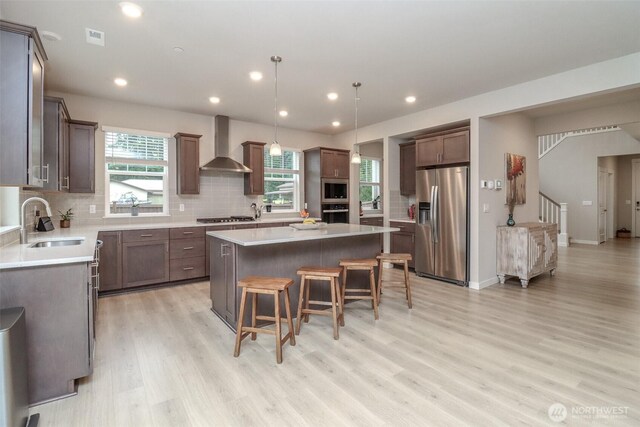 16321 SE 133rd Pl, Renton, WA 98059 - kitchen with wall chimney range hood, stainless steel appliances, a center island, a breakfast bar area, and light wood-style floors