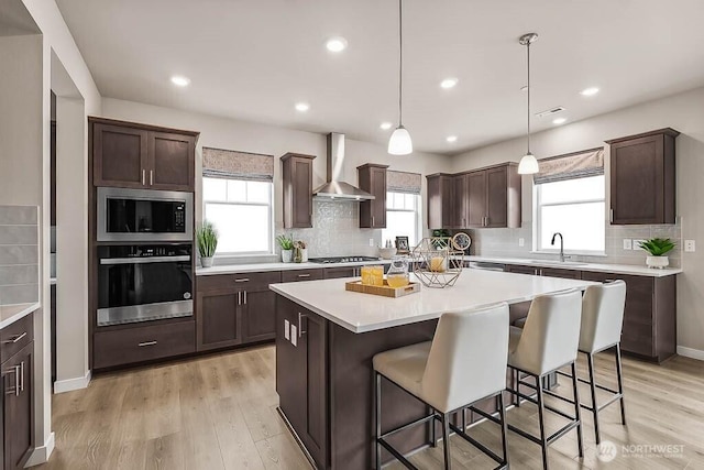 16204 SE 133rd Pl Unit 101, Renton, WA 98059 - kitchen featuring stainless steel appliances, wall chimney exhaust hood, dark brown cabinets, backsplash, and a center island