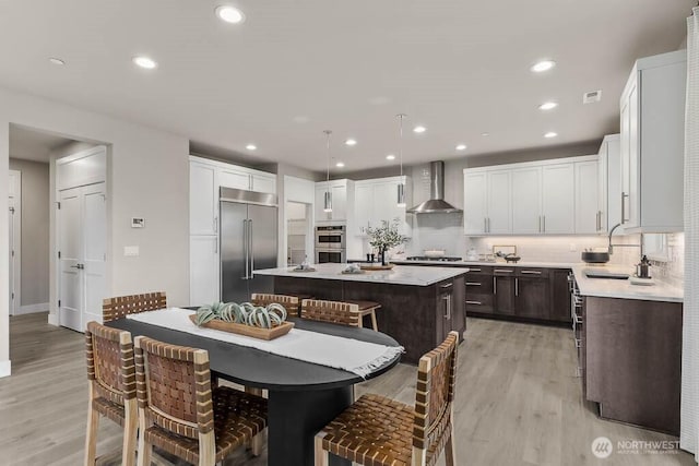 13212 164th Ave SE Unit 207, Renton, WA 98059 - kitchen with stainless steel appliances, wall chimney range hood, a kitchen island, light wood-type flooring, and tasteful backsplash