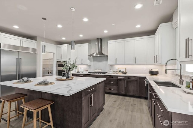 13212 164th Ave SE Unit 207, Renton, WA 98059 - kitchen featuring wall chimney range hood, a kitchen island, dark brown cabinets, appliances with stainless steel finishes, and a kitchen bar