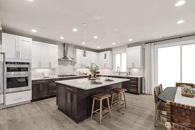 13212 164th Ave SE Unit 207, Renton, WA 98059 - kitchen featuring wall chimney range hood, appliances with stainless steel finishes, a kitchen bar, a center island, and dark brown cabinetry