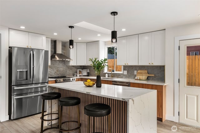 7605 20th Ave E, Tacoma, WA 98404 - kitchen with wall chimney range hood, appliances with stainless steel finishes, light wood finished floors, light stone countertops, and a kitchen island