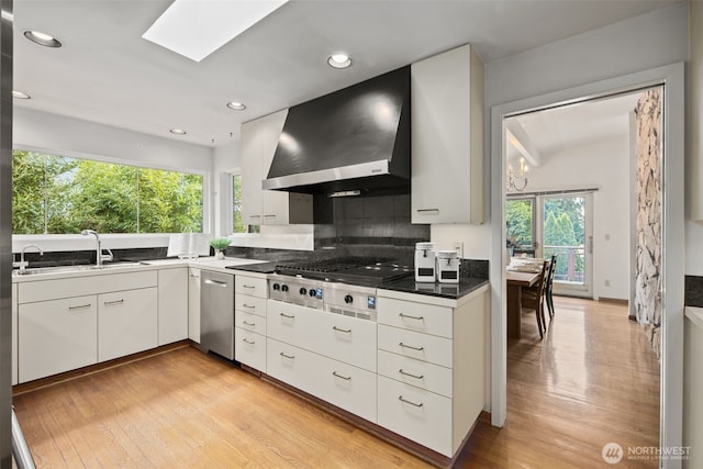 3015 44th Ave W, Seattle, WA 98199 - kitchen featuring wall chimney exhaust hood, appliances with stainless steel finishes, backsplash, a skylight, and light wood-type flooring