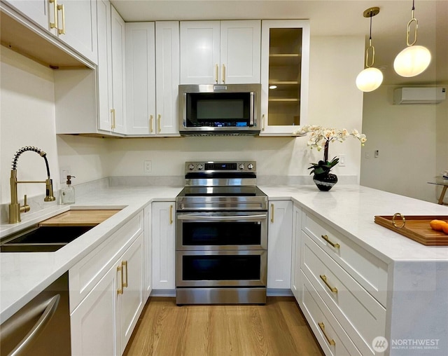 746 N 88th St, Seattle, WA 98103 - kitchen featuring stainless steel appliances, an AC wall unit, a peninsula, light wood-style floors, and white cabinetry