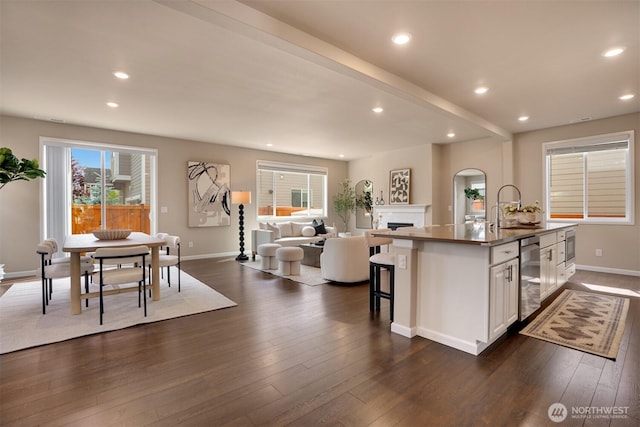 4418 233rd Pl SE, Bothell, WA 98021 - kitchen featuring a fireplace, open floor plan, a kitchen island with sink, dark wood-style flooring, and white cabinets