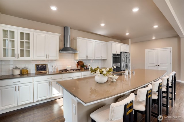 4418 233rd Pl SE, Bothell, WA 98021 - kitchen featuring wall chimney range hood, dark wood-type flooring, appliances with stainless steel finishes, a kitchen island with sink, and white cabinets