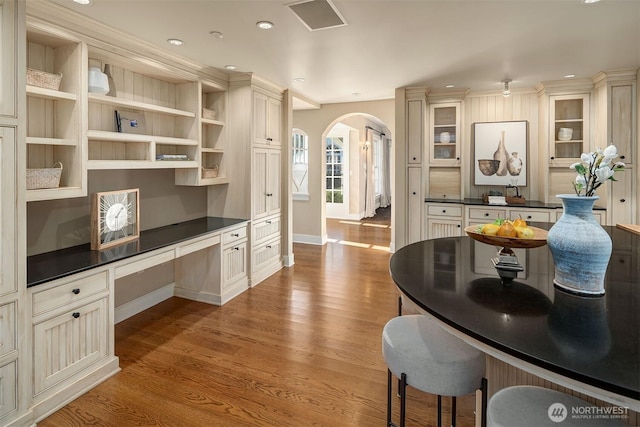 1135 Evergreen Point Rd, Medina, WA 98039 - kitchen with arched walkways, built in desk, dark countertops, wood finished floors, and glass insert cabinets