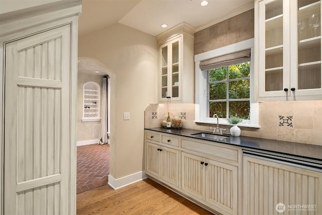 1135 Evergreen Point Rd, Medina, WA 98039 - kitchen featuring cream cabinetry, dark countertops, arched walkways, backsplash, and glass insert cabinets