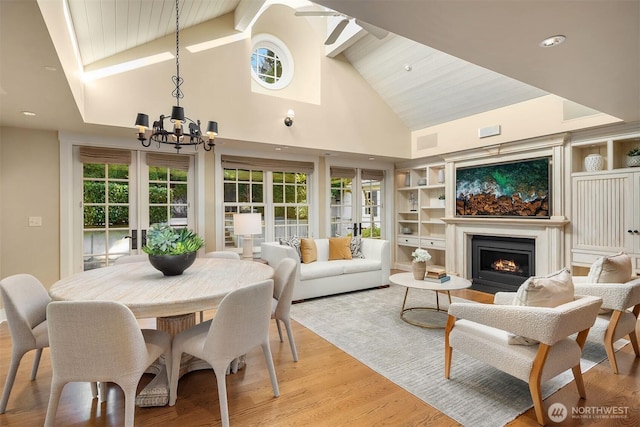 1135 Evergreen Point Rd, Medina, WA 98039 - dining space featuring high vaulted ceiling, a chandelier, light wood finished floors, a lit fireplace, and plenty of natural light