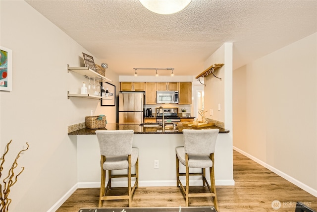 3045 20th Ave W Unit 108, Seattle, WA 98199 - kitchen featuring stainless steel appliances, a peninsula, light wood-type flooring, a kitchen breakfast bar, and open shelves