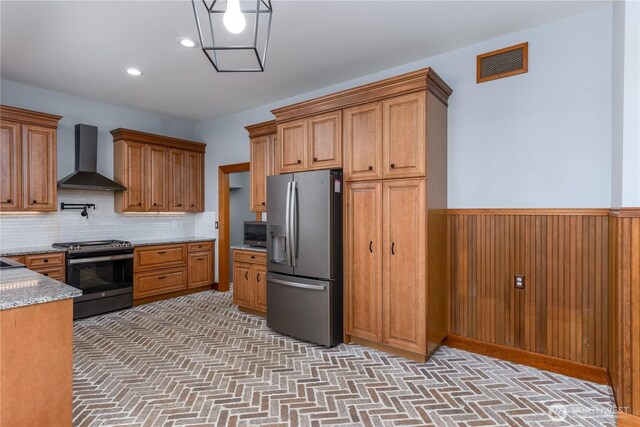 11801 Rd 5.6 NE, Moses Lake, WA 98837 - kitchen featuring appliances with stainless steel finishes, wall chimney range hood, brown cabinetry, decorative backsplash, and wainscoting
