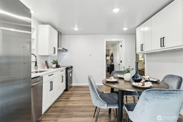 4715 S Cushman Ave, Tacoma, WA 98408 - kitchen with stainless steel appliances, wall chimney range hood, wood finished floors, white cabinetry, and recessed lighting