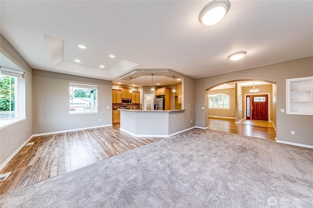 120 Petal Ln, Sequim, WA 98382 - unfurnished living room featuring arched walkways, light colored carpet, light wood-style flooring, a tray ceiling, and recessed lighting