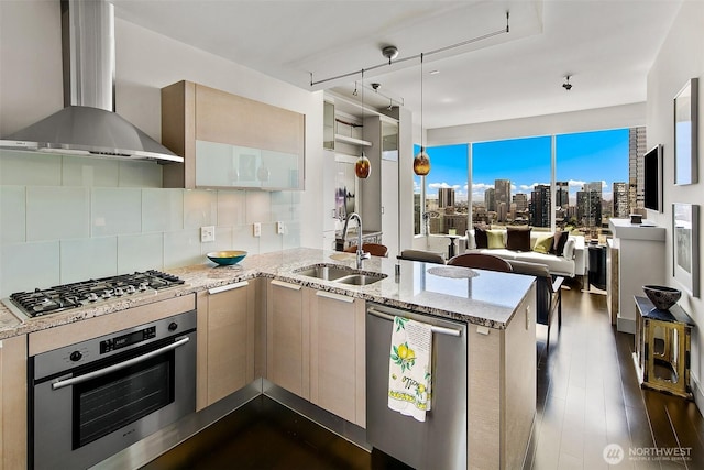 737 Olive Way Unit 3606, Seattle, WA 98101 - kitchen featuring wall chimney range hood, appliances with stainless steel finishes, a peninsula, tasteful backsplash, and light stone countertops