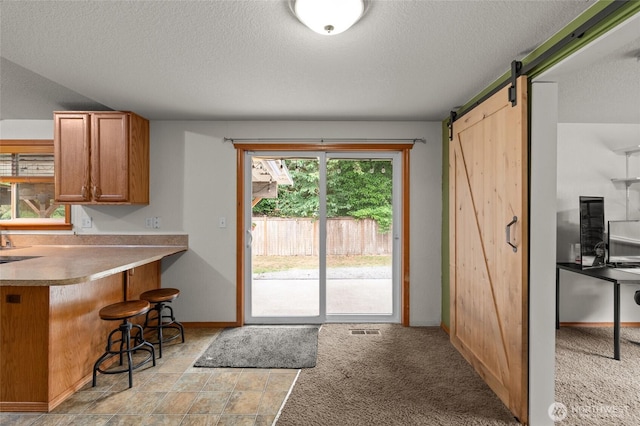 6137 189th Loop SW, Rochester, WA 98579 - kitchen with a barn door, a textured ceiling, a breakfast bar, brown cabinets, and light countertops