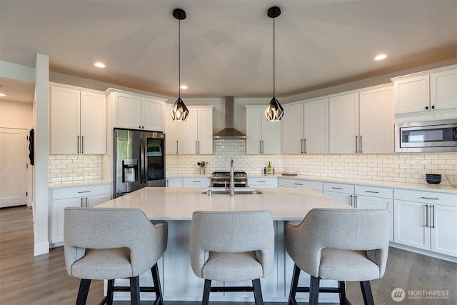2035 S Fruitland, Puyallup, WA 98371 - kitchen featuring wall chimney exhaust hood, appliances with stainless steel finishes, wood finished floors, a kitchen island with sink, and decorative backsplash