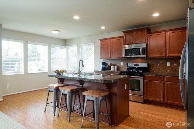 14516 270th Pl NE, Duvall, WA 98019 - kitchen with appliances with stainless steel finishes, dark countertops, a breakfast bar area, tasteful backsplash, and light wood-style floors