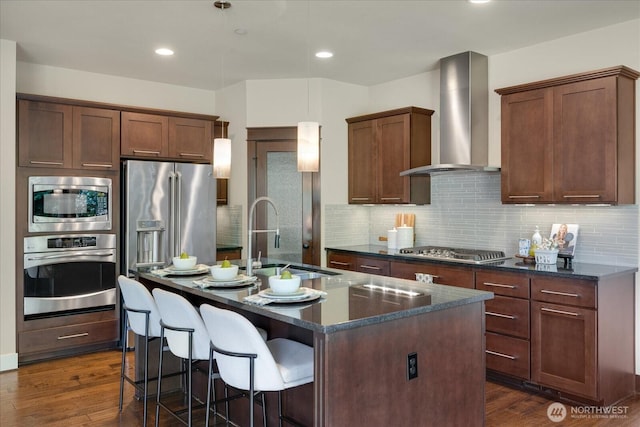 6555 125th Ave NE, Kirkland, WA 98033 - kitchen featuring appliances with stainless steel finishes, wall chimney exhaust hood, dark wood-style flooring, an island with sink, and tasteful backsplash