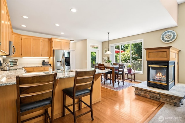 8206 66th Avenue Ct E, Puyallup, WA 98371 - kitchen featuring stainless steel appliances, a peninsula, a multi sided fireplace, light wood finished floors, and light stone counters