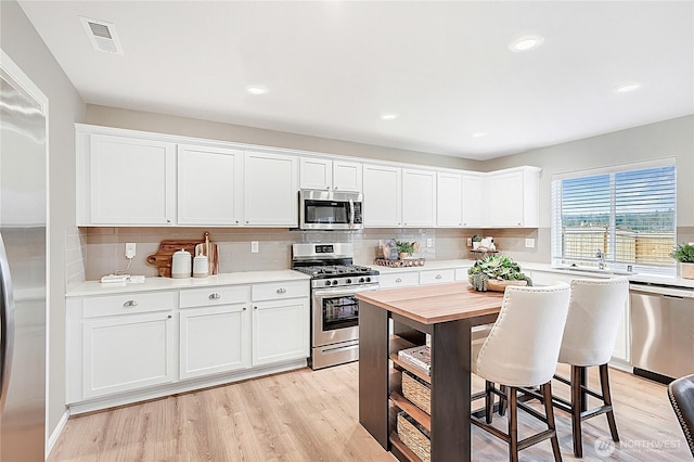 1212 15th Ave, Sultan, WA 98294 - kitchen with appliances with stainless steel finishes, tasteful backsplash, white cabinetry, light wood finished floors, and a breakfast bar area