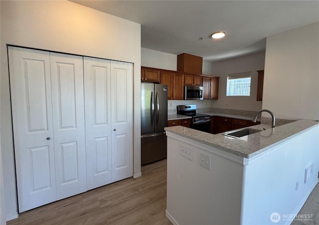 14915 38th Dr SE Unit Ii2051, Bothell, WA 98012 - kitchen featuring appliances with stainless steel finishes, a peninsula, light wood-style floors, light stone counters, and brown cabinetry