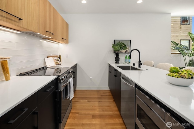 2419 NW 57th Unit B, Seattle, WA 98107 - kitchen featuring appliances with stainless steel finishes, light wood-type flooring, tasteful backsplash, light countertops, and recessed lighting