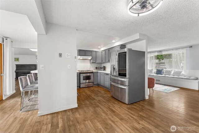 15627 SE 263rd Pl, Covington, WA 98042 - kitchen featuring stainless steel appliances, gray cabinetry, under cabinet range hood, light countertops, and wood finished floors