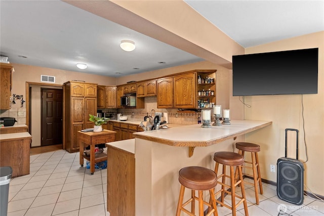 1714 N Astor Ct, East Wenatchee, WA 98802 - kitchen with brown cabinets, stainless steel microwave, light tile patterned floors, a peninsula, and tasteful backsplash