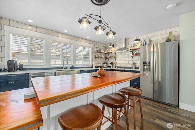 214 S Bradley St, Chelan, WA 98816 - kitchen featuring butcher block countertops, appliances with stainless steel finishes, wall chimney range hood, blue cabinetry, and recessed lighting