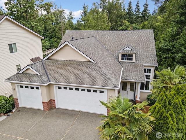 14691 NE 16th St, Bellevue, WA 98007 - view of front of house with an attached garage, roof with shingles, concrete driveway, brick siding, and view of wooded area