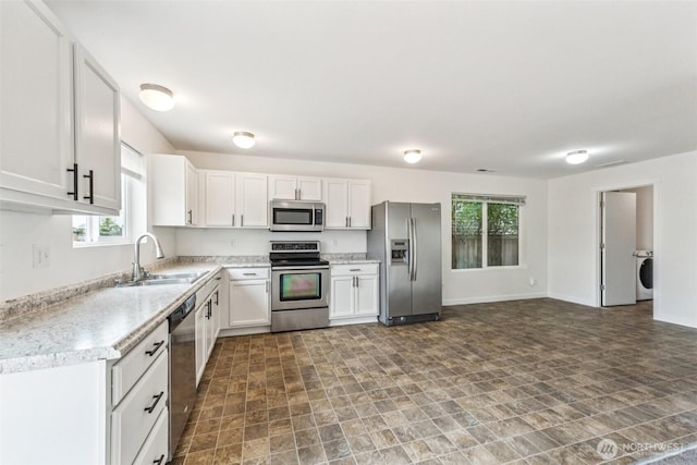 29775 218th Pl SE, Kent, WA 98042 - kitchen featuring appliances with stainless steel finishes, washer / clothes dryer, white cabinetry, light countertops, and stone finish flooring