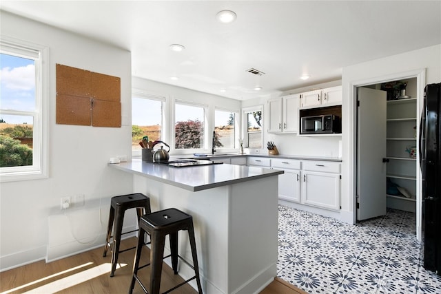 600 SW Cloverdale St, Seattle, WA 98106 - kitchen with a breakfast bar, a peninsula, white cabinetry, freestanding refrigerator, and recessed lighting