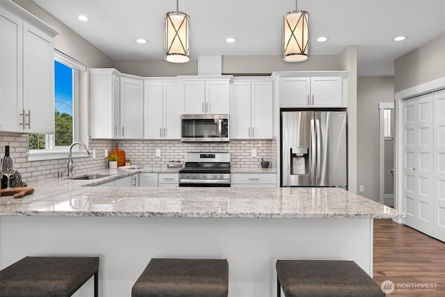5690 Sunstone Pl Unit 101, Ferndale, WA 98248 - kitchen featuring stainless steel appliances, a peninsula, white cabinetry, light stone countertops, and hanging light fixtures