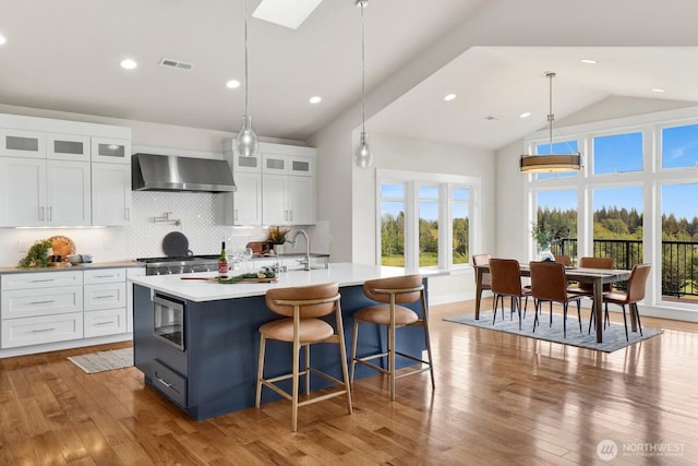 5754 W 26th Crst, Ferndale, WA 98248 - kitchen with wall chimney exhaust hood, stainless steel microwave, light countertops, white cabinets, and a center island with sink
