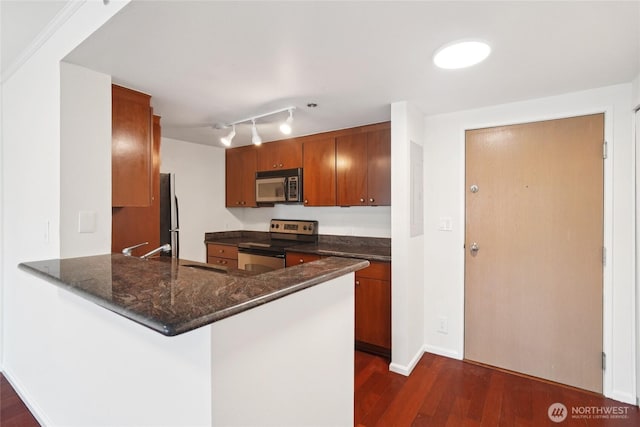 121 Vine St Unit 402, Seattle, WA 98121 - kitchen with appliances with stainless steel finishes, dark wood-style flooring, brown cabinets, a peninsula, and dark stone counters