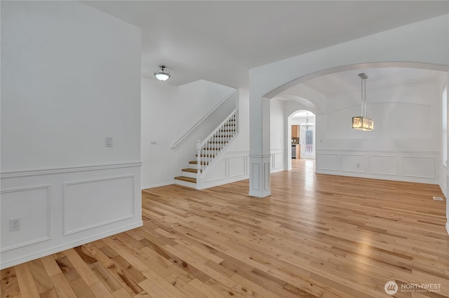 7003 Radius Loop SE, Lacey, WA 98513 - unfurnished living room with arched walkways, a decorative wall, light wood-style flooring, stairway, and a wainscoted wall
